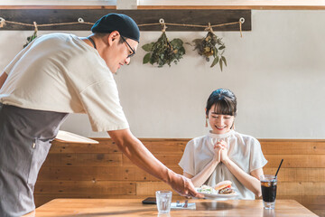 ランチを食べにカフェ・飲食店に来たアジア人女性と料理を運ぶ配膳する男性店員・スタッフ
