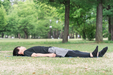 Fototapeta premium 公園でヨガマットをひいてヨガ・ピラティスをする若い男性 