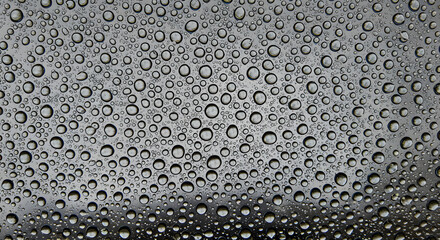 Close-up perpendicular shot of a water droplet-covered glass surface, with light refractions creating a unique texture