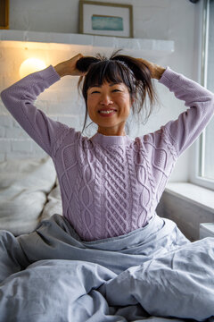 Cheerful young woman tying hair while waking up in bed