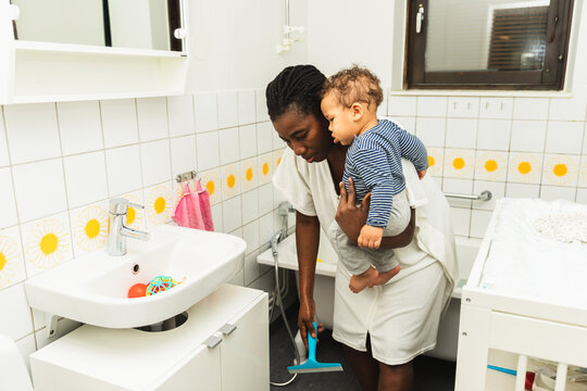 Mother Holding Baby While Cleaning Wet Floor After Shower at Home
