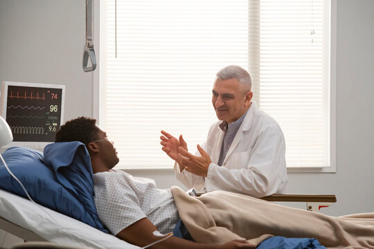 Senior doctor explaining diagnosis to patient in hospital bed