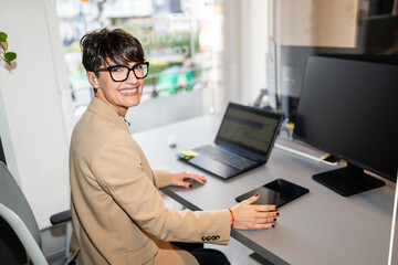 Happy businesswoman working with laptop and tablet in coworking space