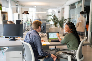 Coworkers sharing statistics on laptop in modern office