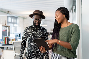 Colleagues using digital tablet, discussing work in coworking space