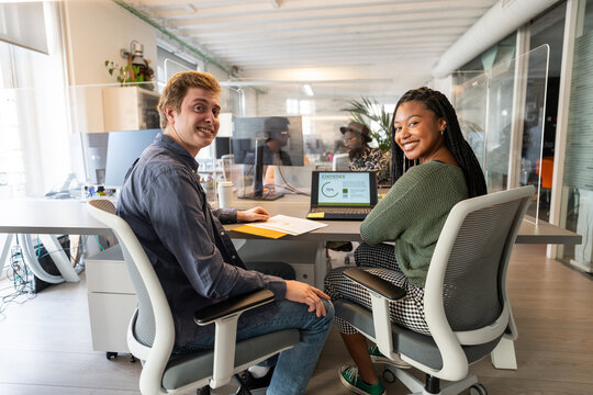 Coworkers smiling at coworking space using laptop