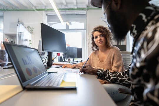 Coworkers discussing charts and data on laptop in modern office