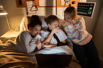 Teenage girls watching funny videos on laptop in hospital room