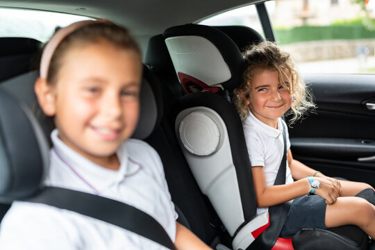 Two smiling school students sitting in booster seats inside car