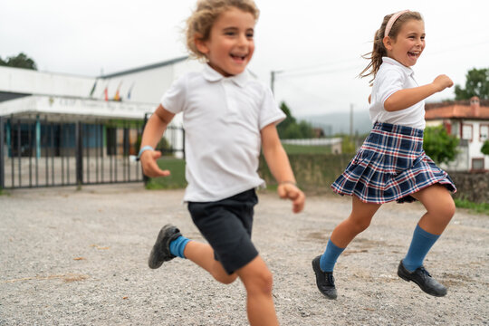 Two happy school kids running outside their school