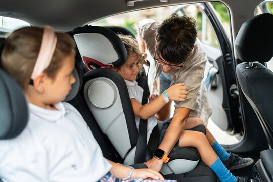 Mother fastening seat belt for daughter in car while going to school