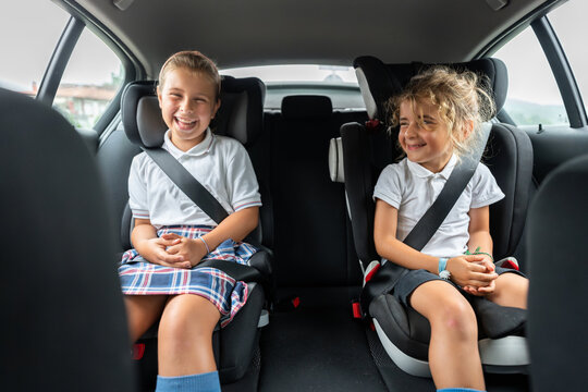 Two cheerful school kids wearing uniform sitting in a car on back seat