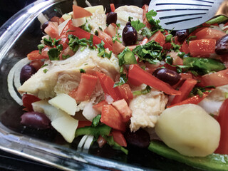 Traditional Portuguese dish of salted cod with black olives, green and red peppers, tomatoes, and potatoes, served in a rustic plate with vibrant colors.