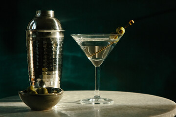Dirty vodka martini with olives and silver shaker in dramatic light