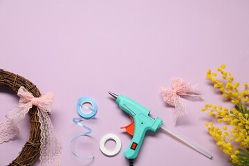 Hot glue gun and handicraft materials on lilac background, flat lay. Space for text