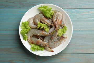 Fresh raw shrimps and lettuce on light blue wooden table, top view