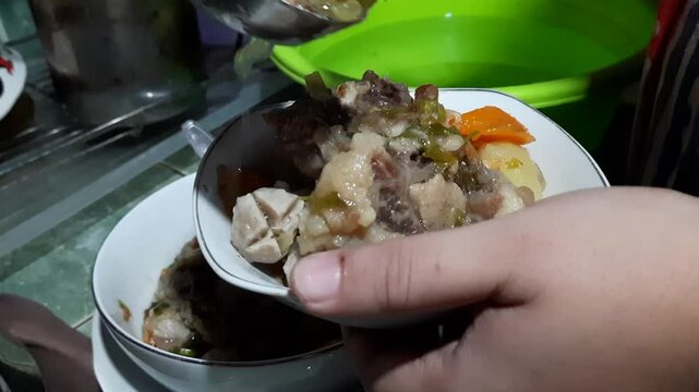 close up of hands scooping oxtail soup into bowls for serving
