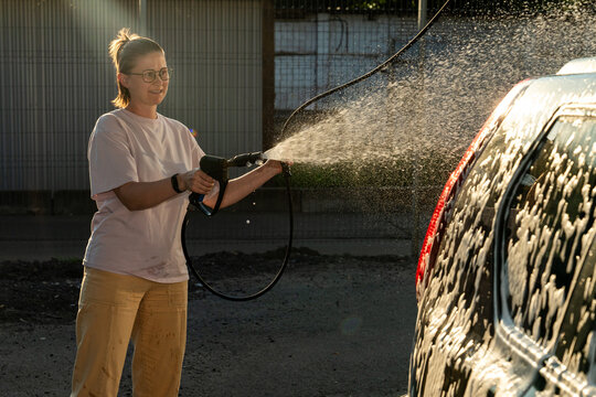 Woman Spraying Water on Soapy Car