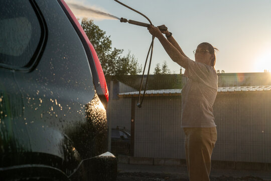 Woman Spraying Water on Car in Sunset
