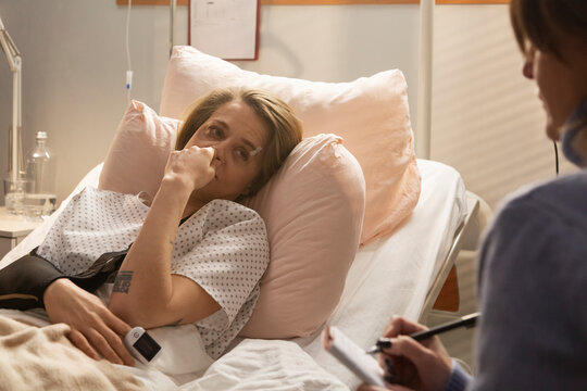 Sick woman lying in hospital bed talking to doctor taking notes