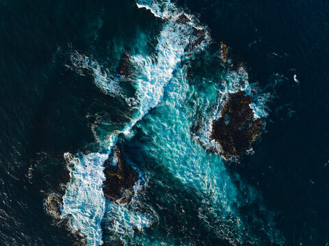 Top down aerial view of ocean wave crashing on coastline at sunset 
