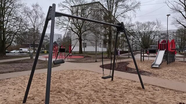 Empty playground during rain, wet surface and overcast sky, urban park scene with gloomy atmosphere as single seat swings