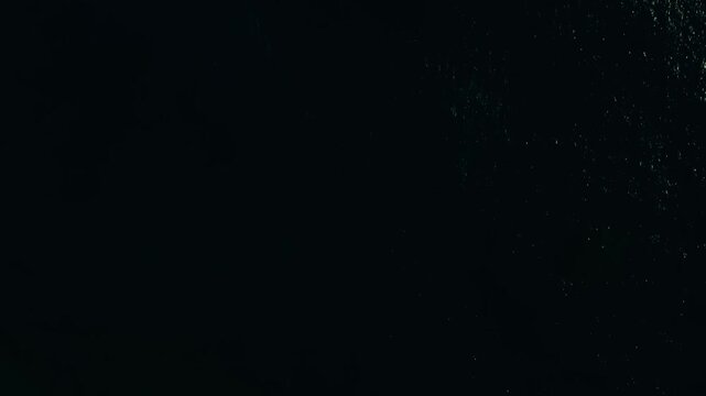 Aerial view of deep, dark ocean water with faint waves and scattered reflections, creating a mysterious and moody atmosphere.