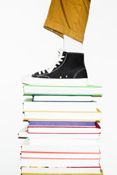 Stack of books and person with sneaker standing on it. Modern office 