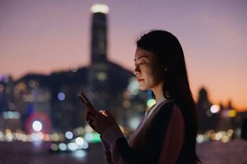 Woman Using Smartphone with City Lights at Dusk