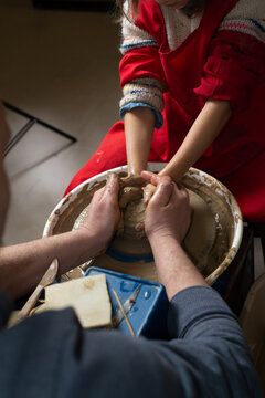 Faceless Master teaches a child to work with clay on a potter's wheel