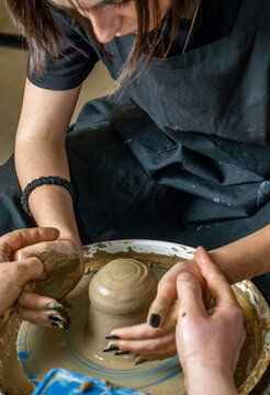 Hands of a master and student on clay on a potter's wheel