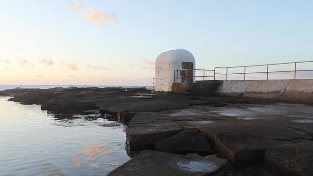 Breathtaking footage of the historic Merewether Pump House silhouetted against a stunning sunrise on the New South Wales coastline. Waves crash gently against the rugged shoreline.