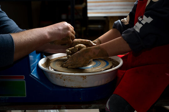 Children's and adults' hands in clay, clay plate on a potter's wheel