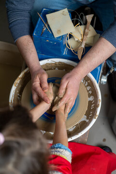 Faceless Master teaches a child to work with clay on a potter's wheel