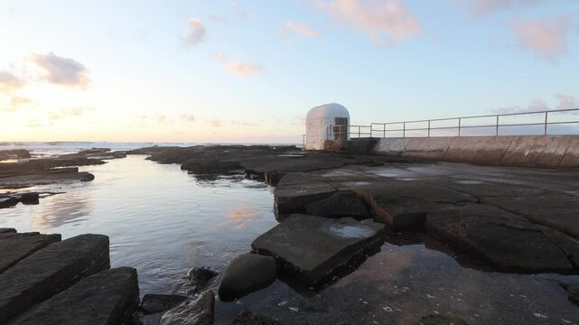 Breathtaking footage of the historic Merewether Pump House silhouetted against a stunning sunrise on the New South Wales coastline. Waves crash gently against the rugged shoreline.