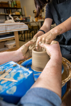 Hands of a master and student on clay on a potter's wheel