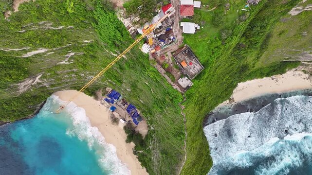 Crane operation over Kelingking Beach, controversial construction project for boost tourism. Drone