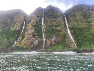 Waterfalls streaming off huge green cliffs into the ocean below on Hawaii's rugged North Kohala Coast