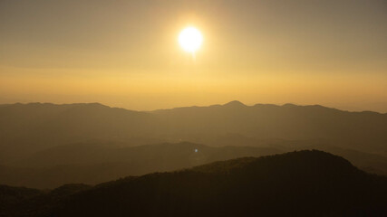 Obraz premium Beautiful sunset in the winter mountains. The setting sun shines down on a serene mountain landscape covered with tropical trees in the evening.