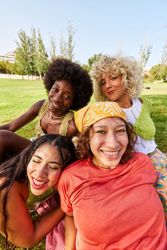 Happy diverse women friends sitting closely in park