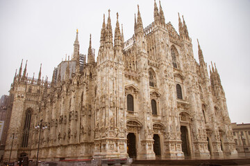 The magnificent exterior of the Milan Cathedral, featuring its Gothic spires and detailed façade under an overcast sky.