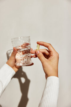 Crop woman with fish oil pill and glass of water