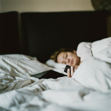 Woman using smartphone in bed with cozy white bedding
