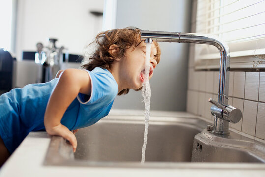 Young boy drinks water directly from kitchen sink at home