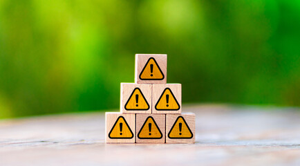 Wooden blocks arranged in pyramid shape displaying yellow warning signs with exclamation marks against blurred green background. Concept of risk management, danger alerts, and safety awareness.