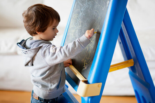 Boy engaged in writing on chalkboard at home during the day