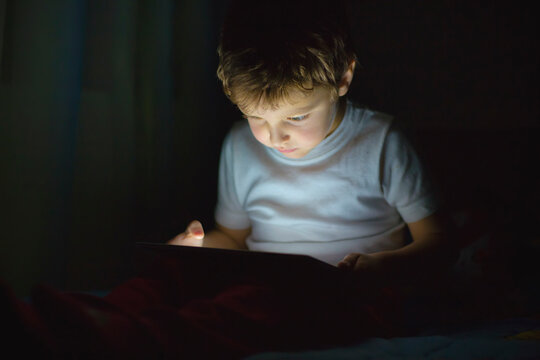 Young boy intently focused on digital tablet in dim light