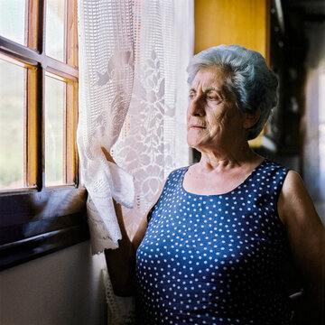 Senior woman gazing thoughtfully out the window in her home