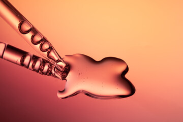 Close up of a pipette dispensing liquid on orange yellow background.