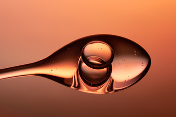 Droplet of fluid gel on orange and yellow gradient backdrop.